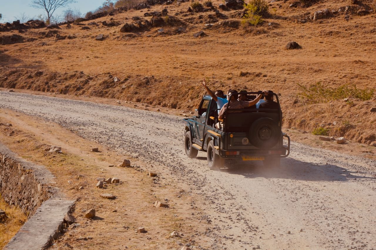 Visitors riding in an open safari jeep along a dusty road through dry, rocky hills