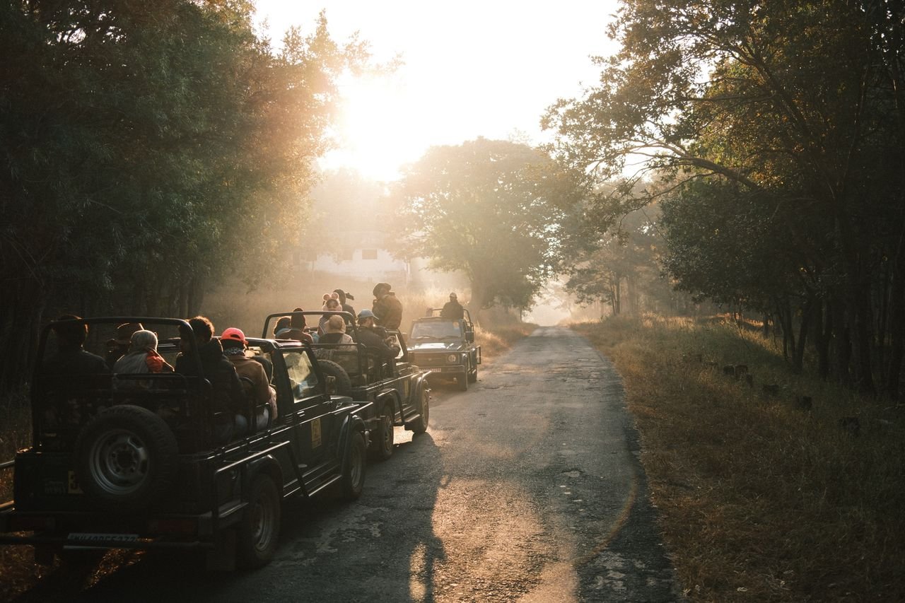 Visitors wearing casual clothing in an open safari jeep on a dusty road through dry, rocky hills