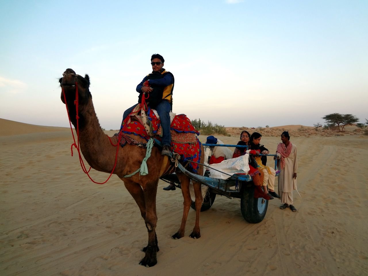 Camel rider beside a passenger cart and handler in the Jaisalmer desert
