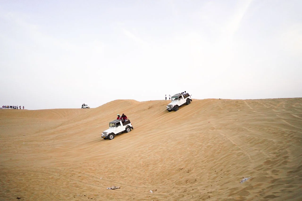 White safari jeeps descending a broad sand dune