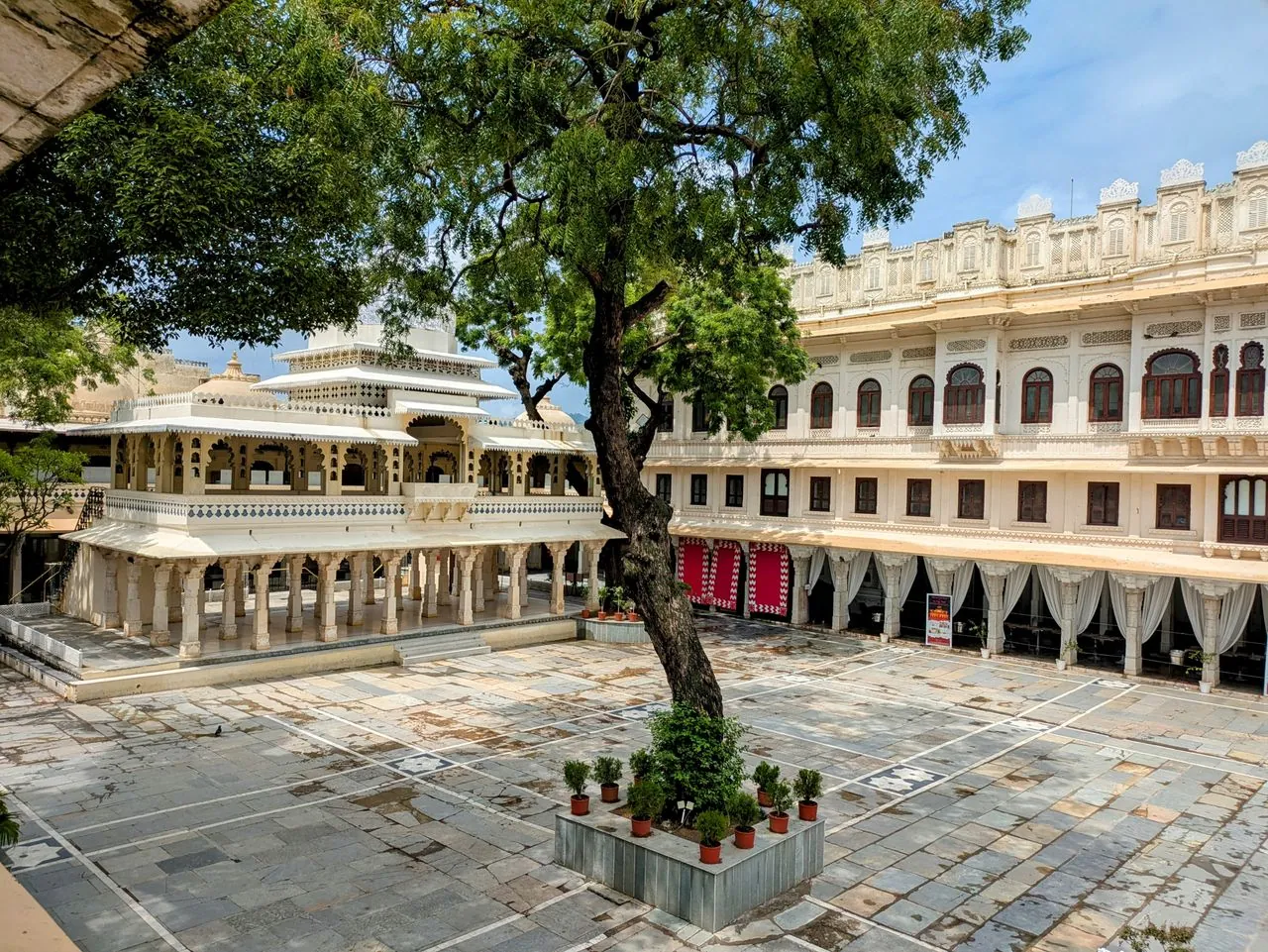 Palace courtyard with a white pavilion, ornate balconies and a large tree