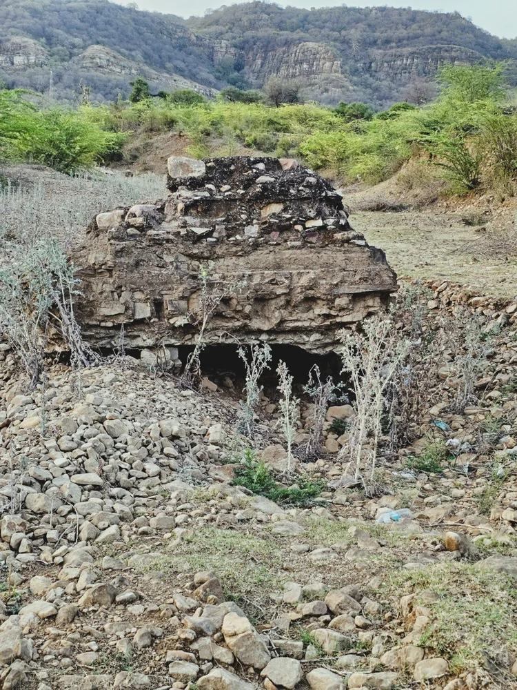 Weathered stone ruins among rocks and scrub with hills behind