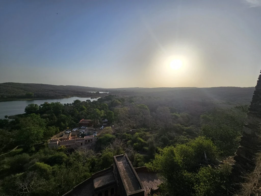Low sun above wooded hills and a lake with stone structures in the foreground
